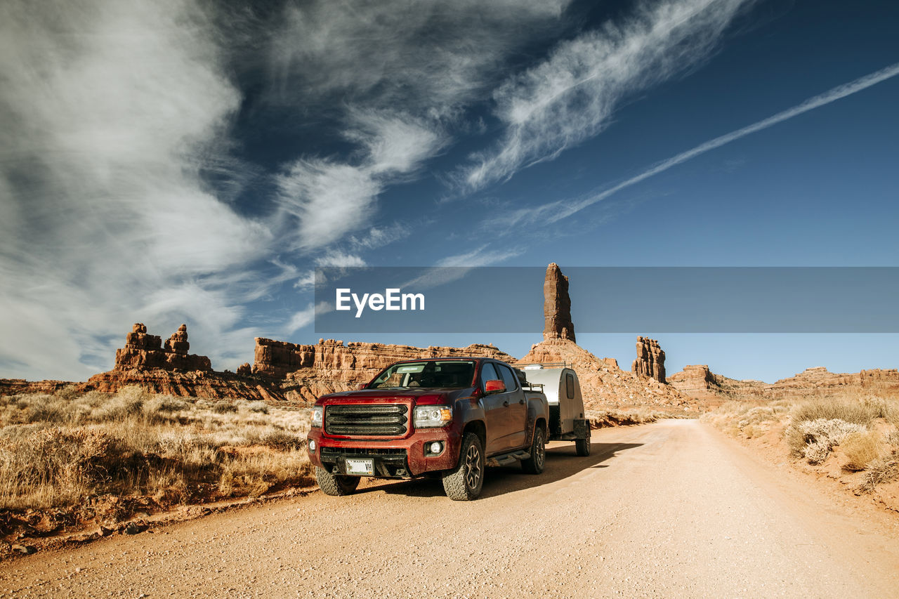 Red truck towing camper along dirt road at valley of the gods, utah