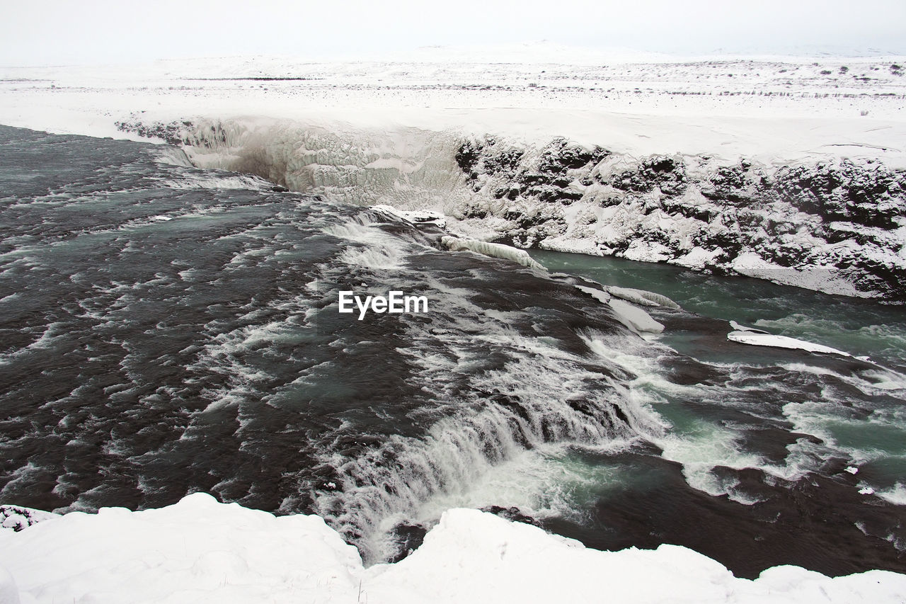 High angle view of flowing river amidst field during winter