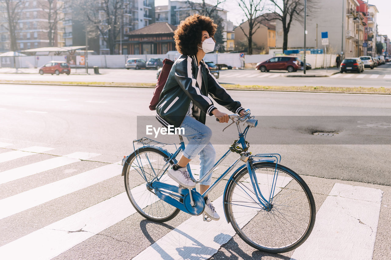 Young woman with face mask and backpack riding bicycle in city