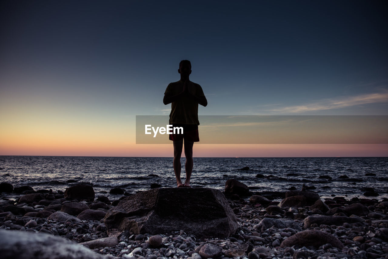 Full length of man exercising at beach against sky during sunset