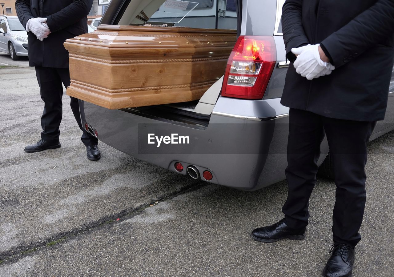 Low section of men standing amidst casket in van on road