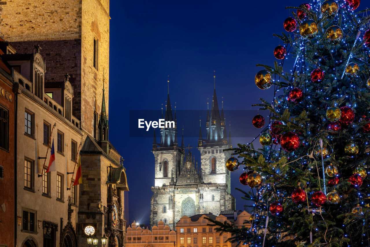 Low angle view of decorated christmas tree and tyn church against blue sky at night