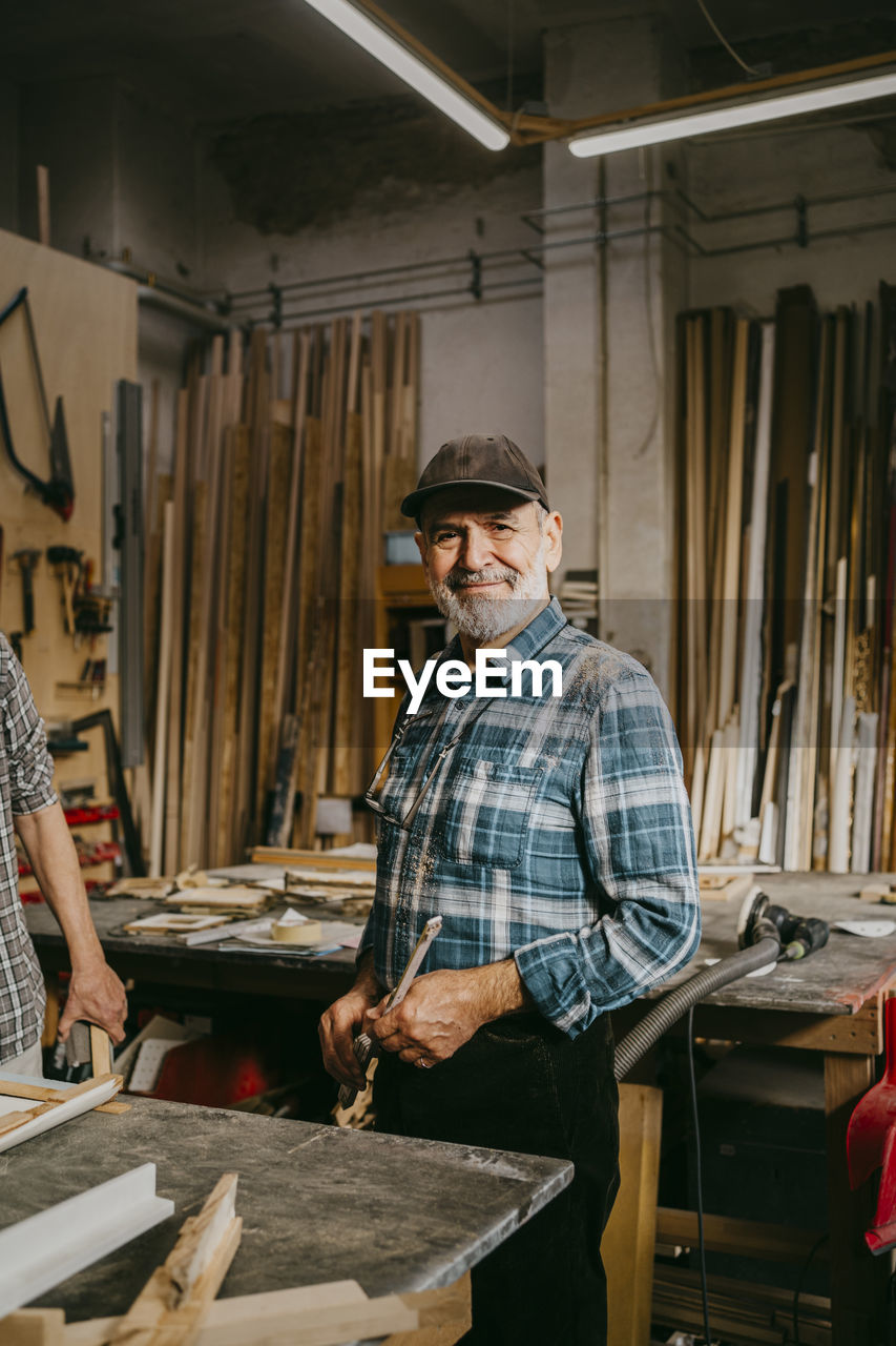 Portrait of smiling senior craftsman standing at workshop