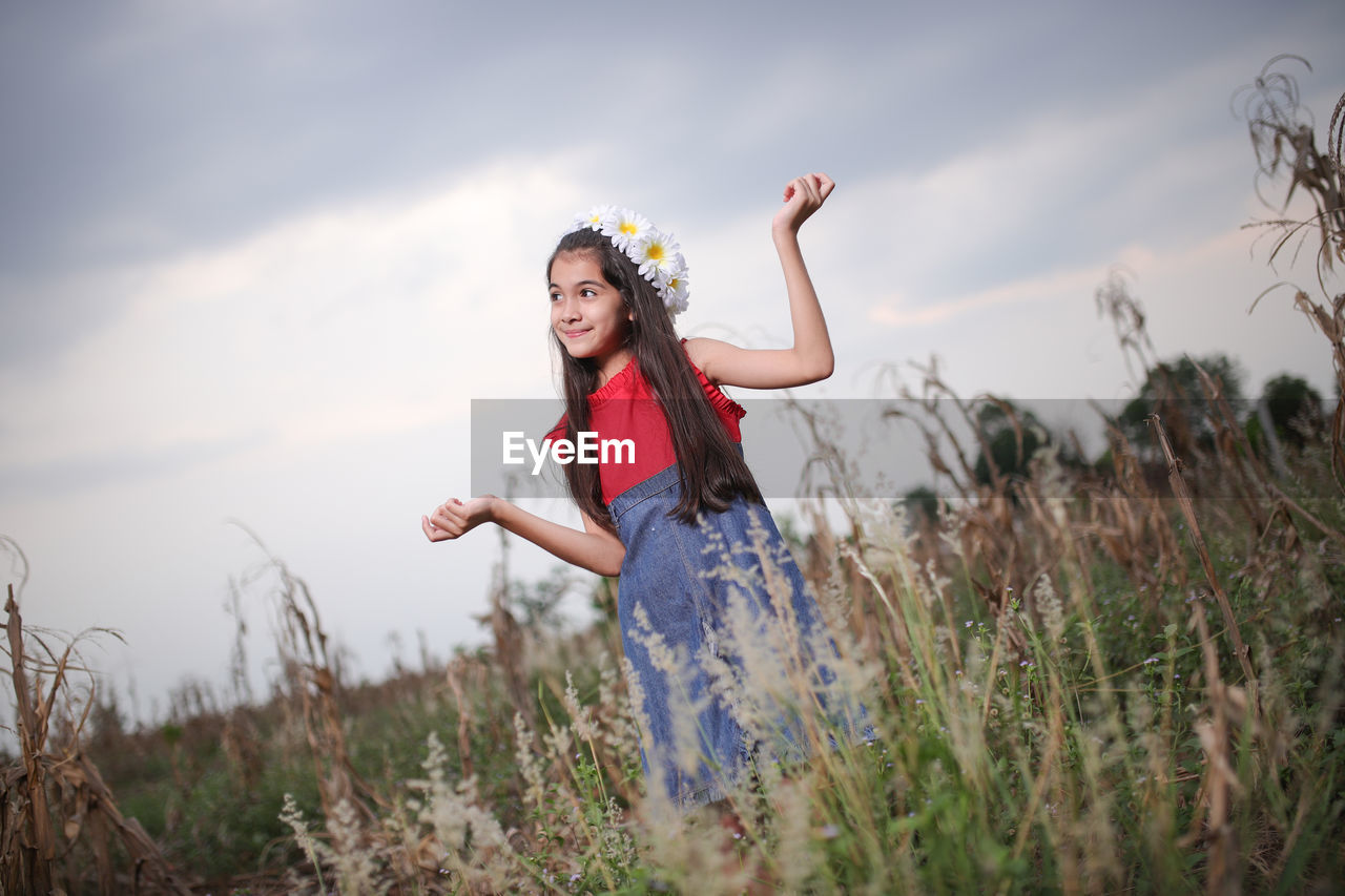 Smiling cute girl standing amidst plants on field during sunset