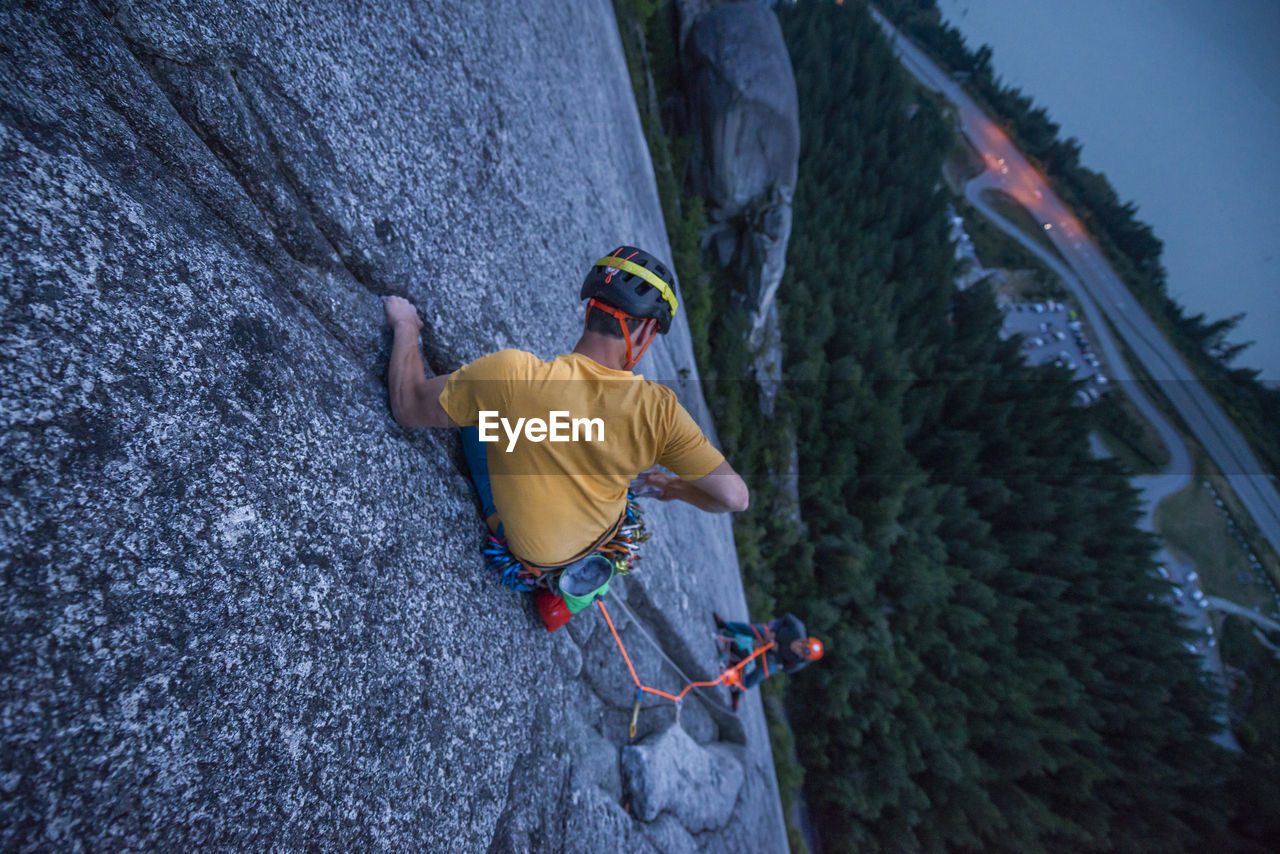 Top view man rock climbing at sunset above the sea and highway