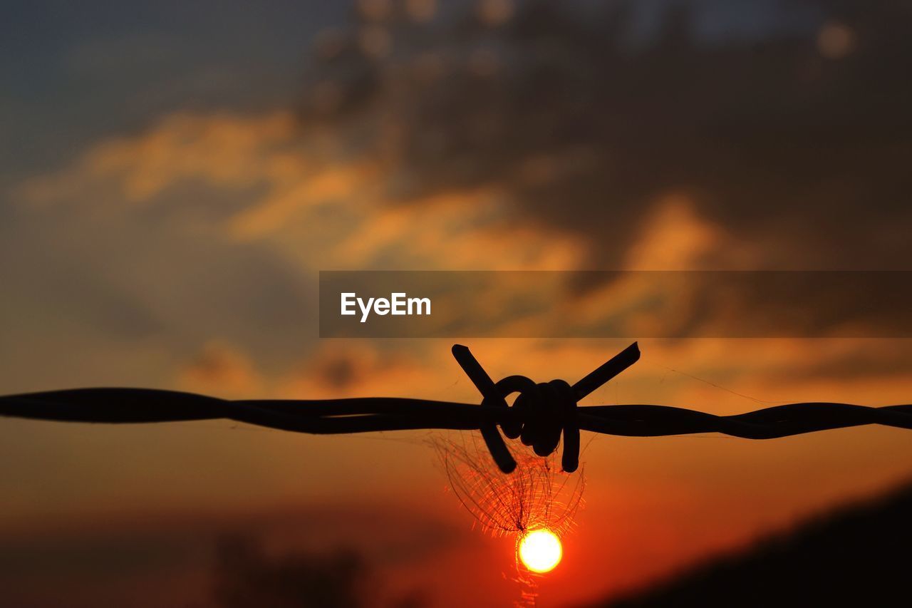 LOW ANGLE VIEW OF SILHOUETTE BARBED WIRE AGAINST SKY DURING SUNSET