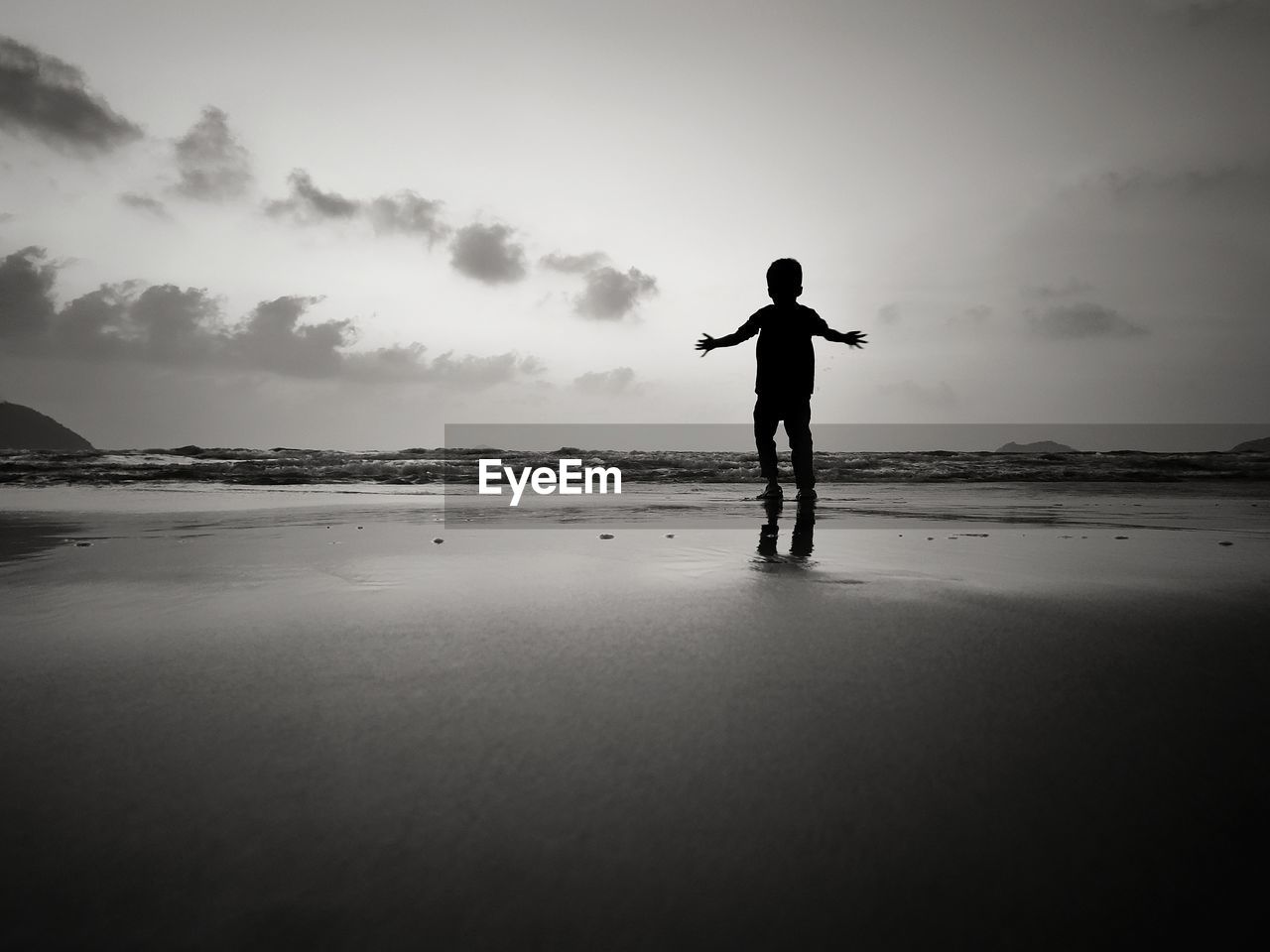 Rear view of silhouette boy standing at beach against sky