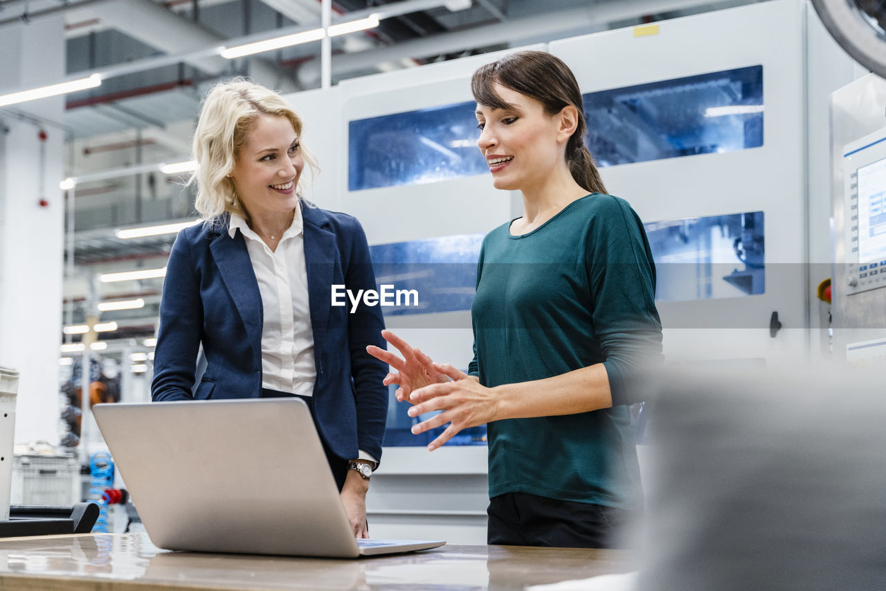 Businesswoman having discussion with colleague over laptop at factory