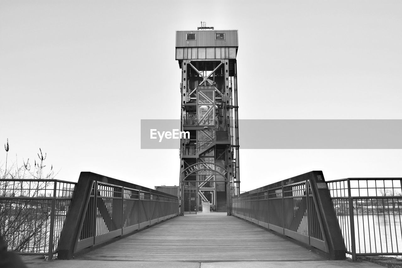 Bridge over canal leading towards buildings against clear sky
