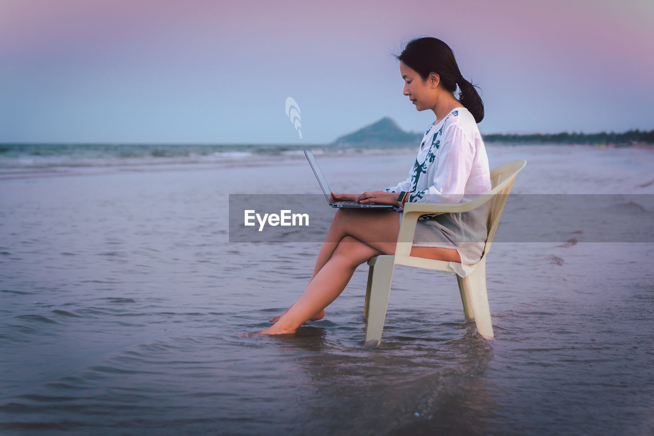 Side view businesswoman using laptop while sitting in a chaie on the beach.
