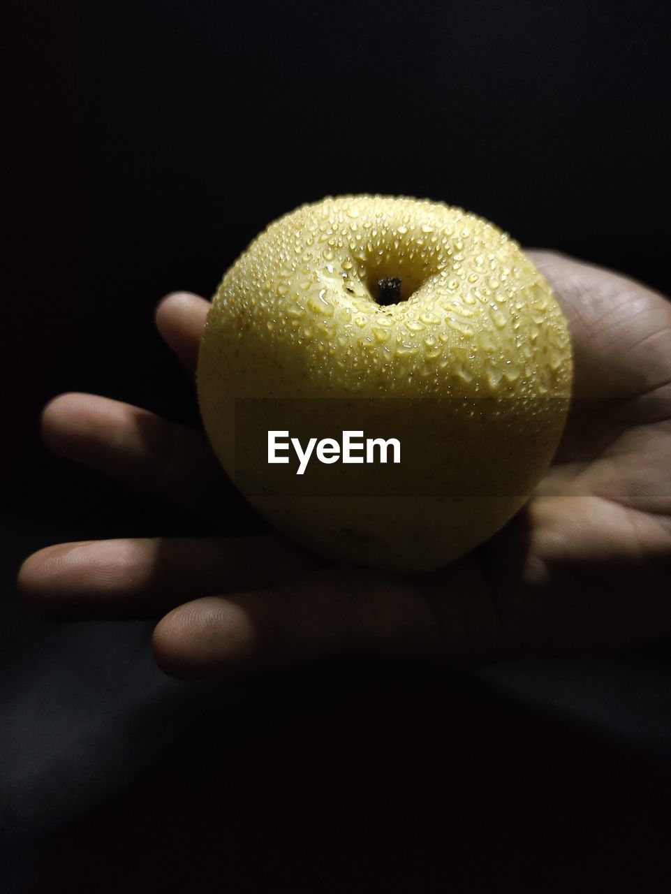 Close-up of hand holding pear against black background