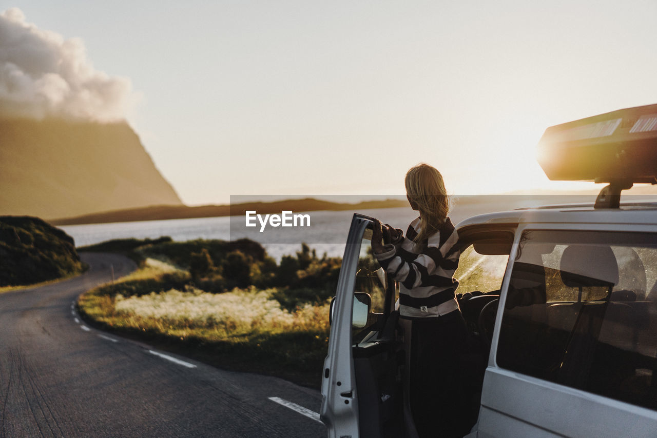 Woman standing by car on road during sunset