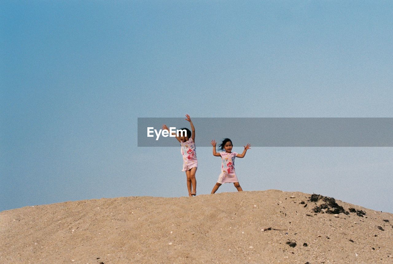 Siblings on sand at beach against clear sky