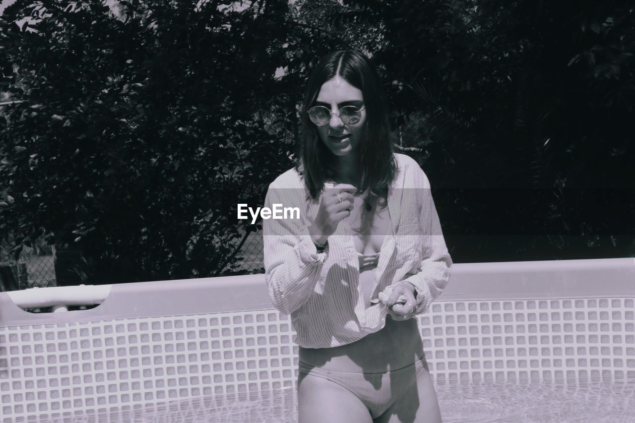 Beautiful woman wearing shirt over bikini in swimming pool during sunny day