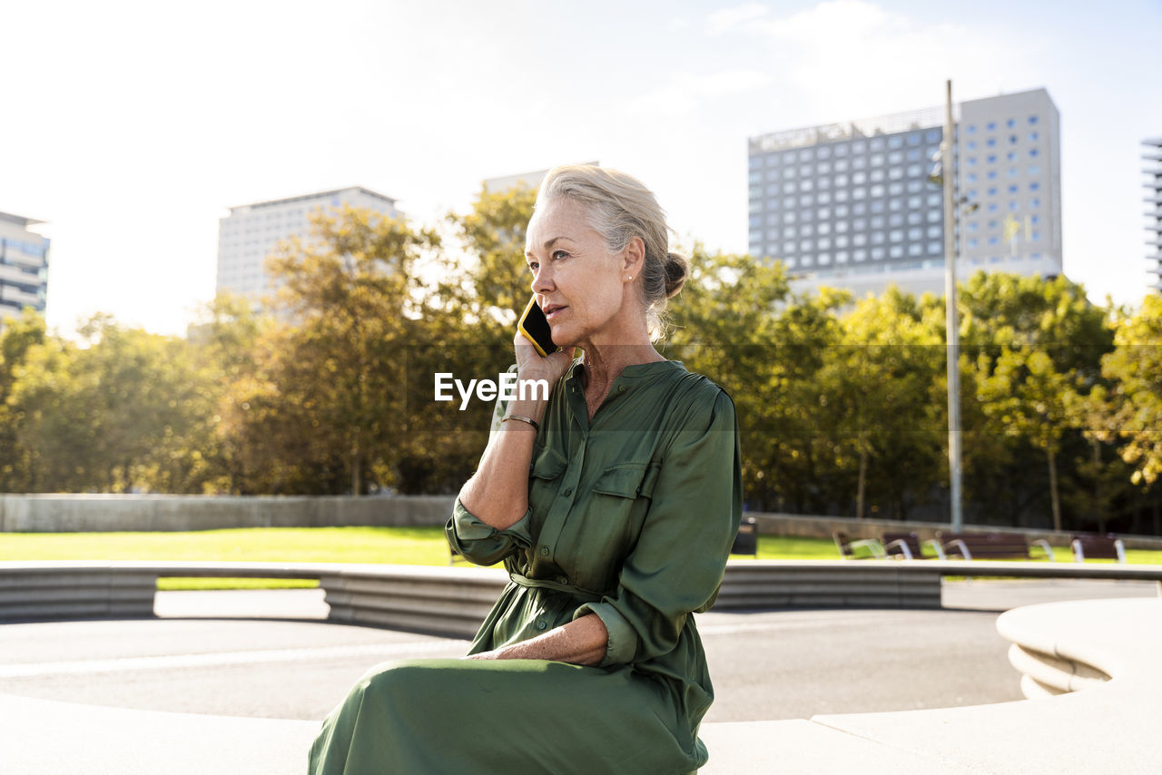 Thoughtful mature woman talking through smart phone sitting on bench