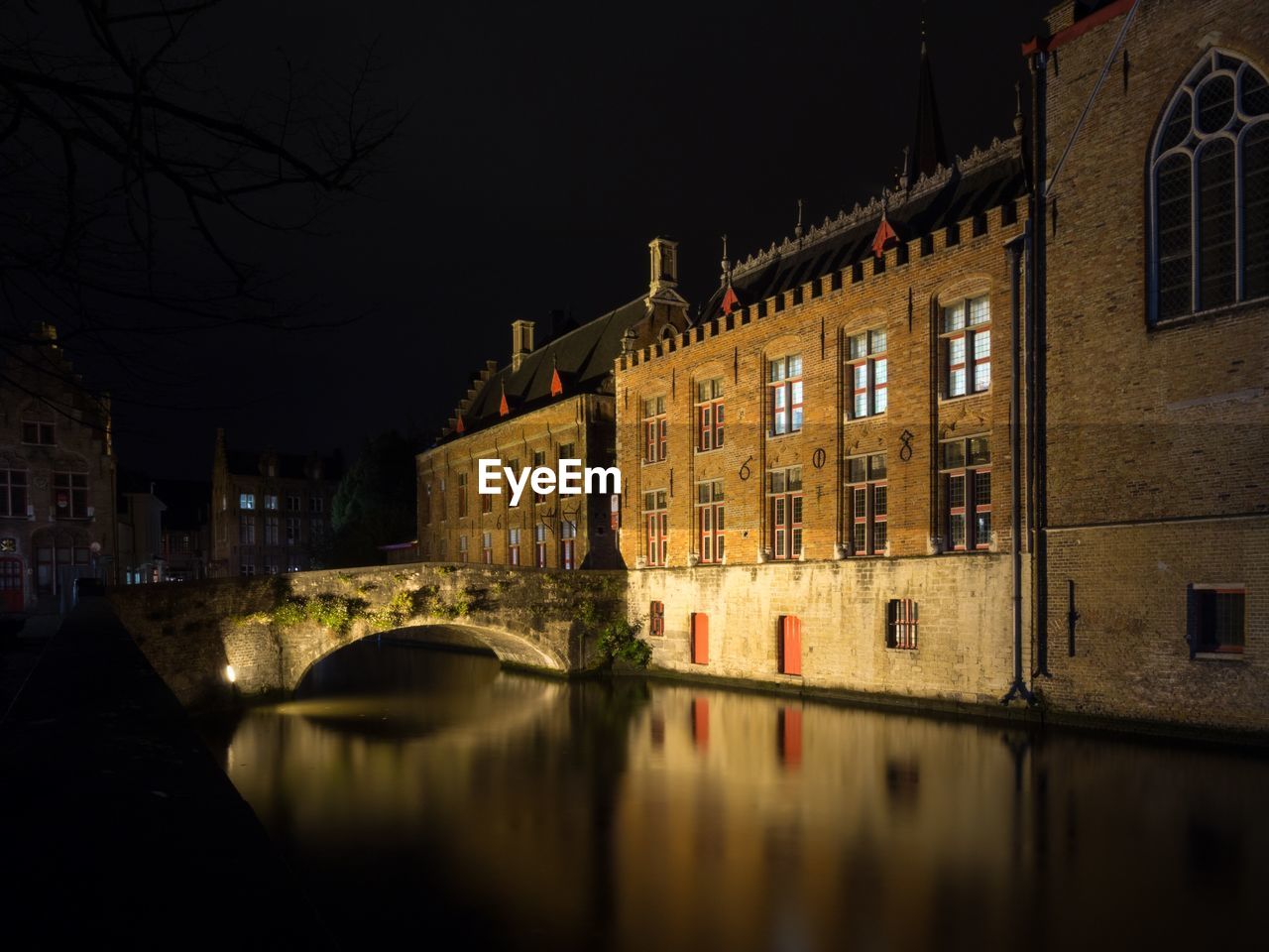 Canal by illuminated buildings in city at night