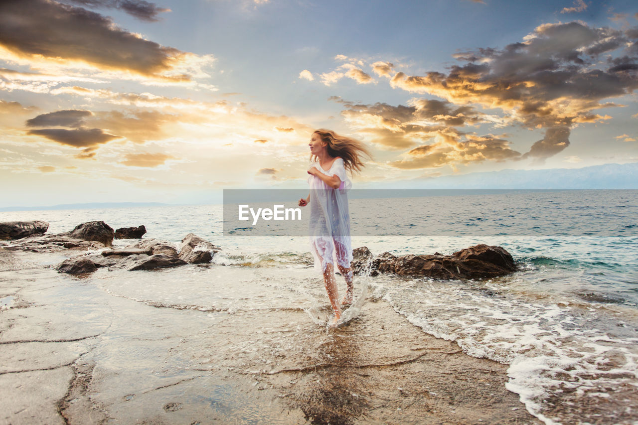 Man standing on rock by sea against sky during sunset