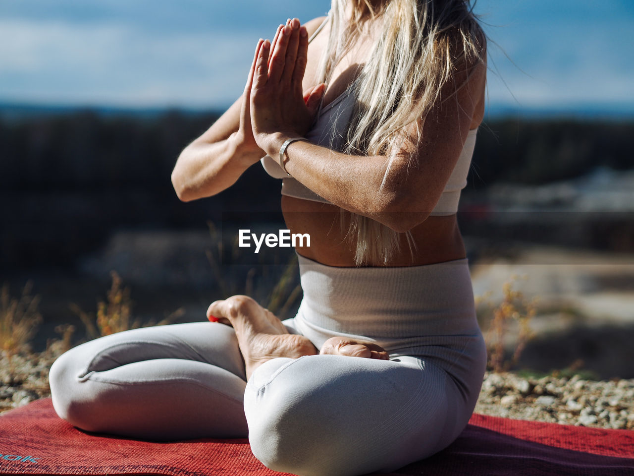 Young beautiful blond woman with long hair in activewear sitting in a lotus pose in a hill