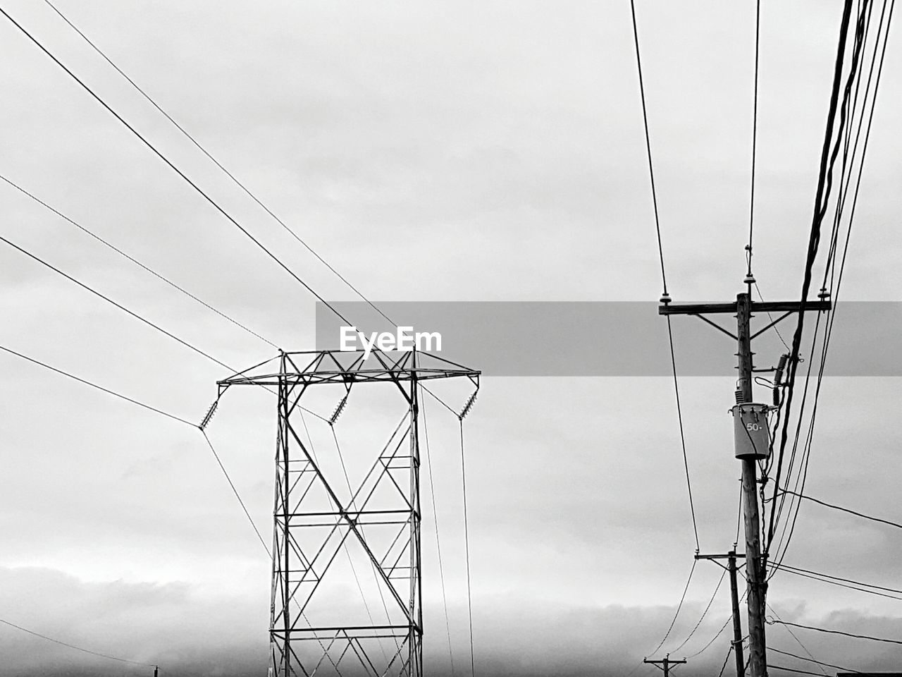 Low angle view of electricity pylons against cloudy sky