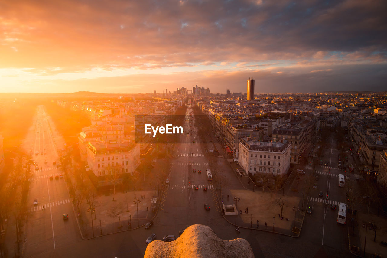 Drone view of urban house facades and roadways with transport under shiny cloudy sky at sundown in paris france