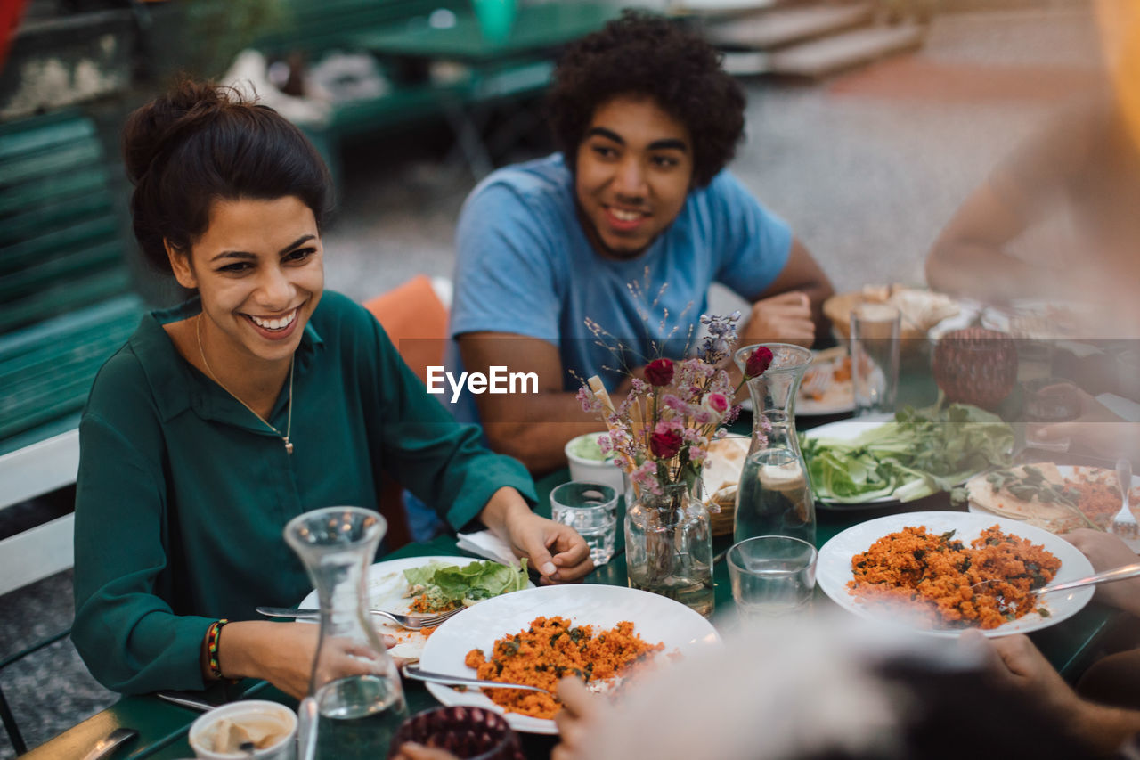 Smiling young woman looking away while enjoying dinner with male friend during garden party