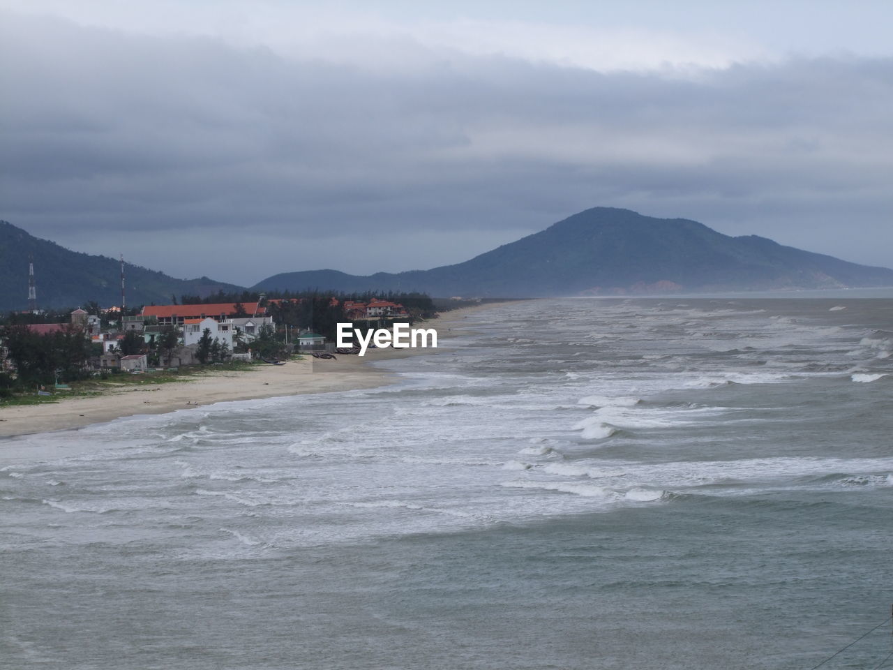 Scenic view of mountain range and coastline against cloudy sky