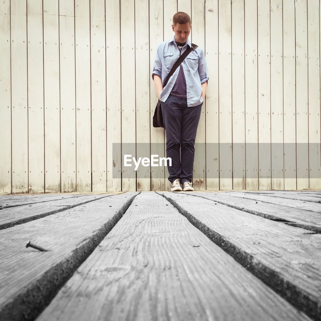 Full length of man standing on wooden boardwalk against wall