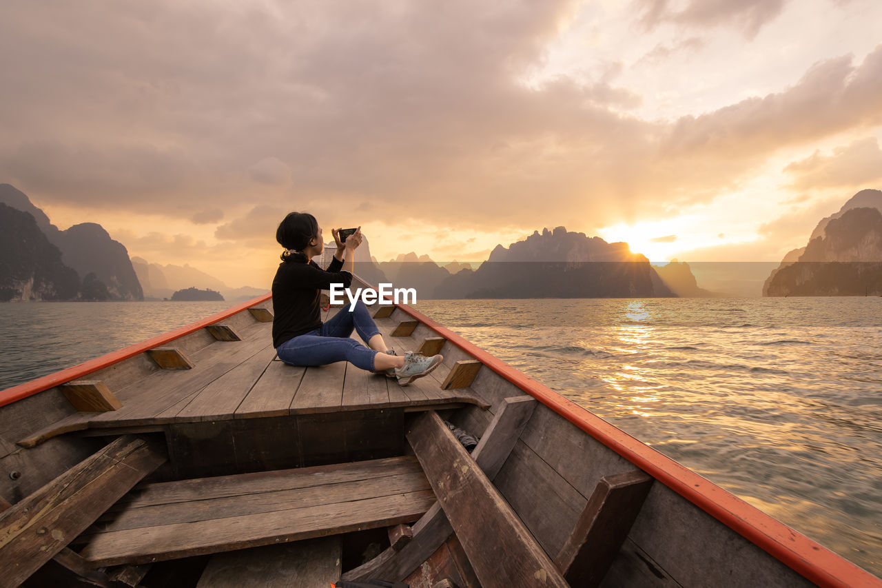 Man sitting on boat in sea against sky during sunset