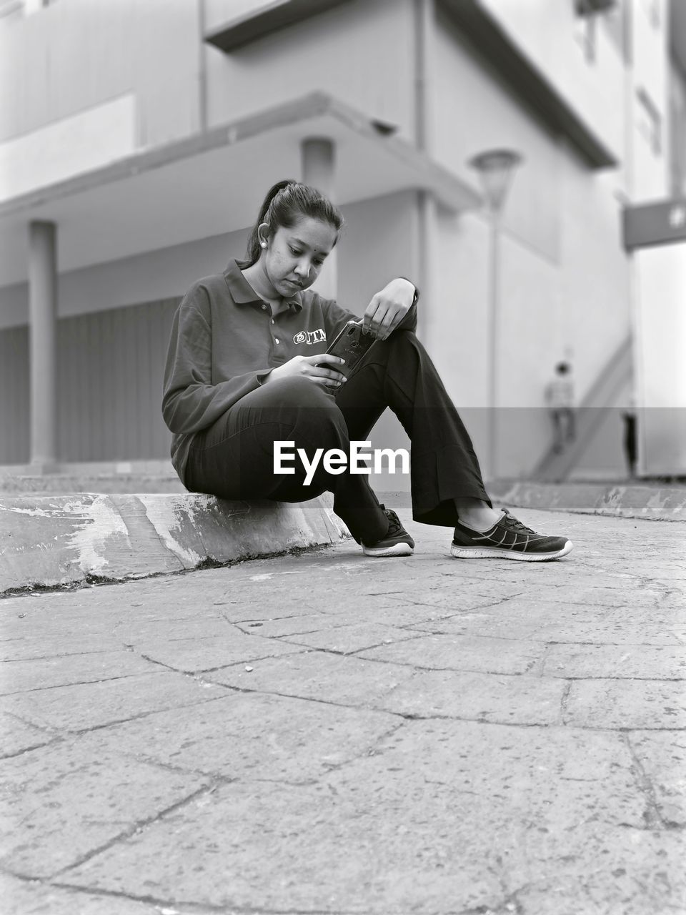 Young woman using phone while sitting on footpath in city