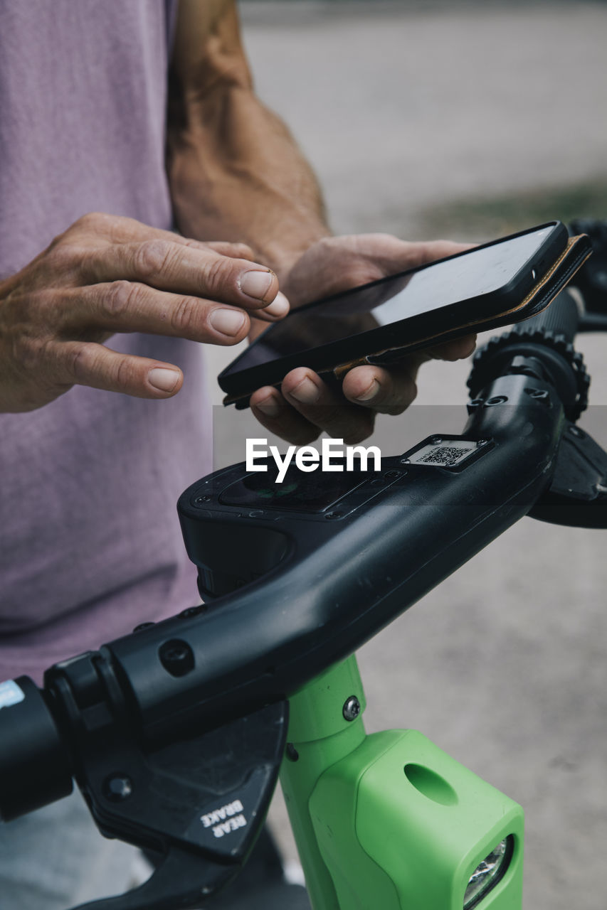 Close-up of hands using smart phon to unlock electric push scooter