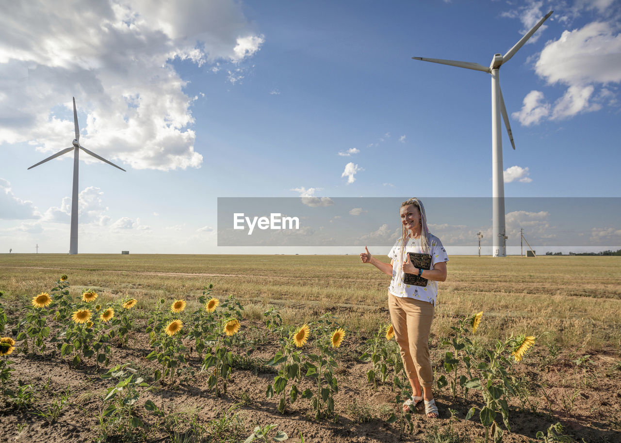 Smiling blogger girl with bright braids shoots story about green energy, wind energy, wind turbines