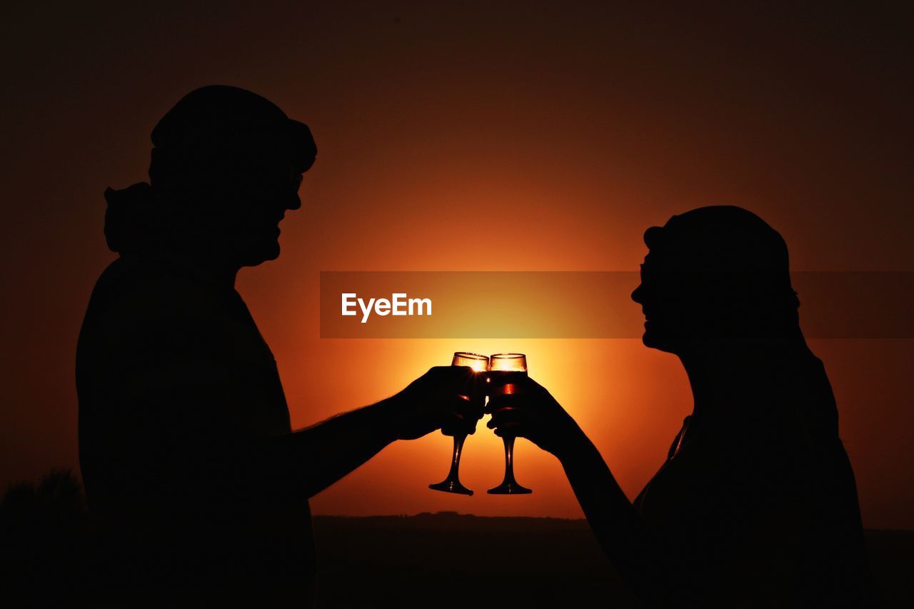 Silhouette couple toasting against orange sky