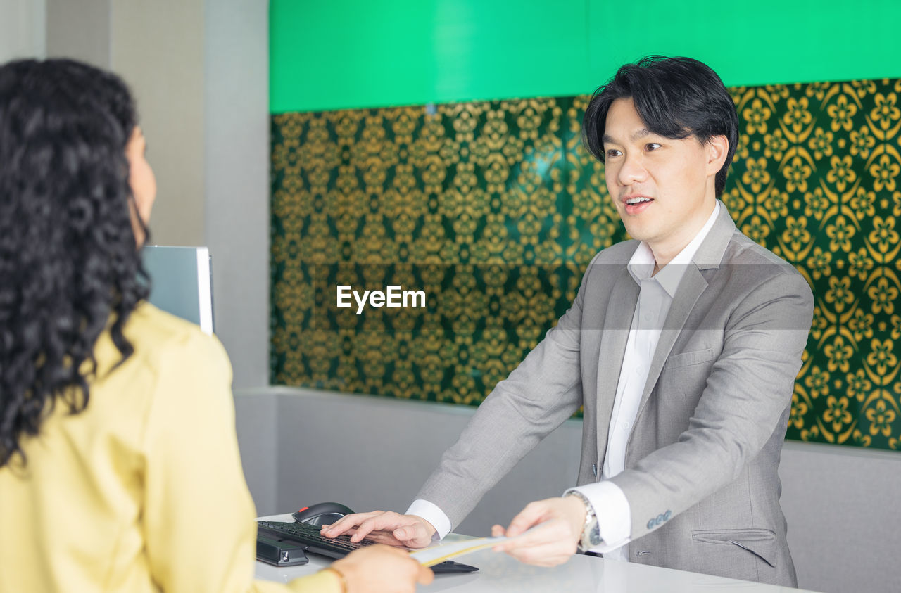 At the airport check-in counter, a passenger hands over his documents to the manager via a counter 