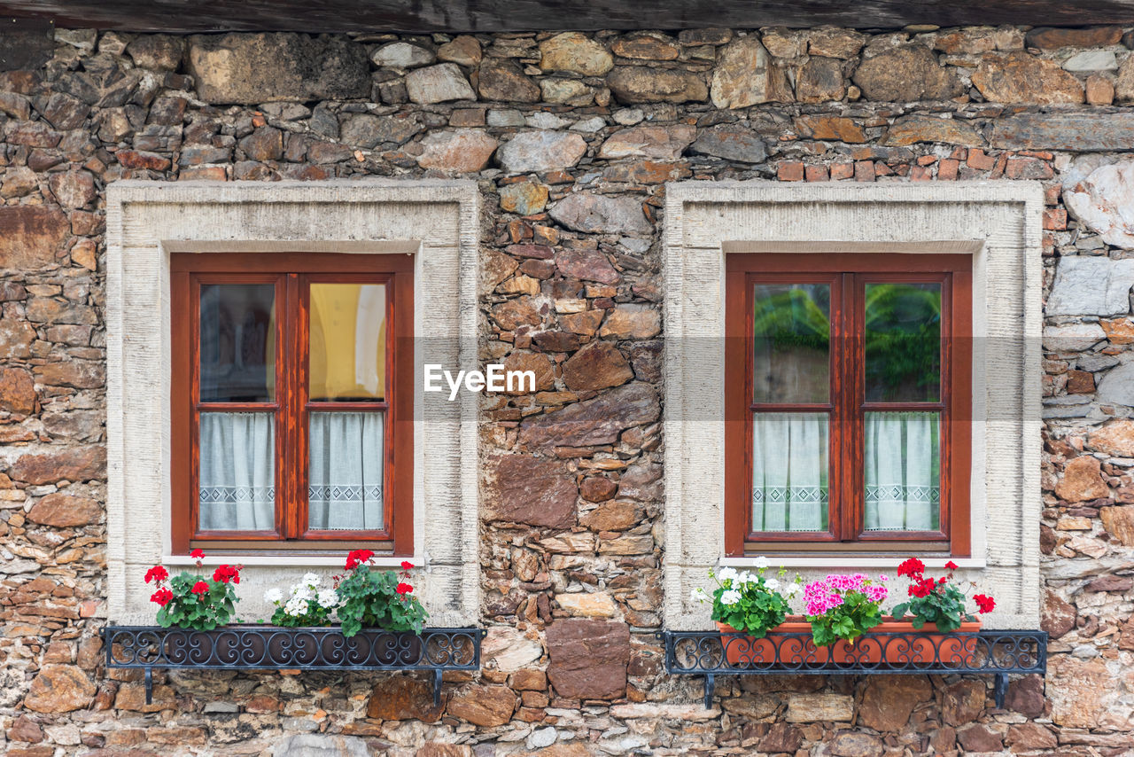 A wooden, brown windows and a fragment of a stone wall of the building. curtains hanging in window