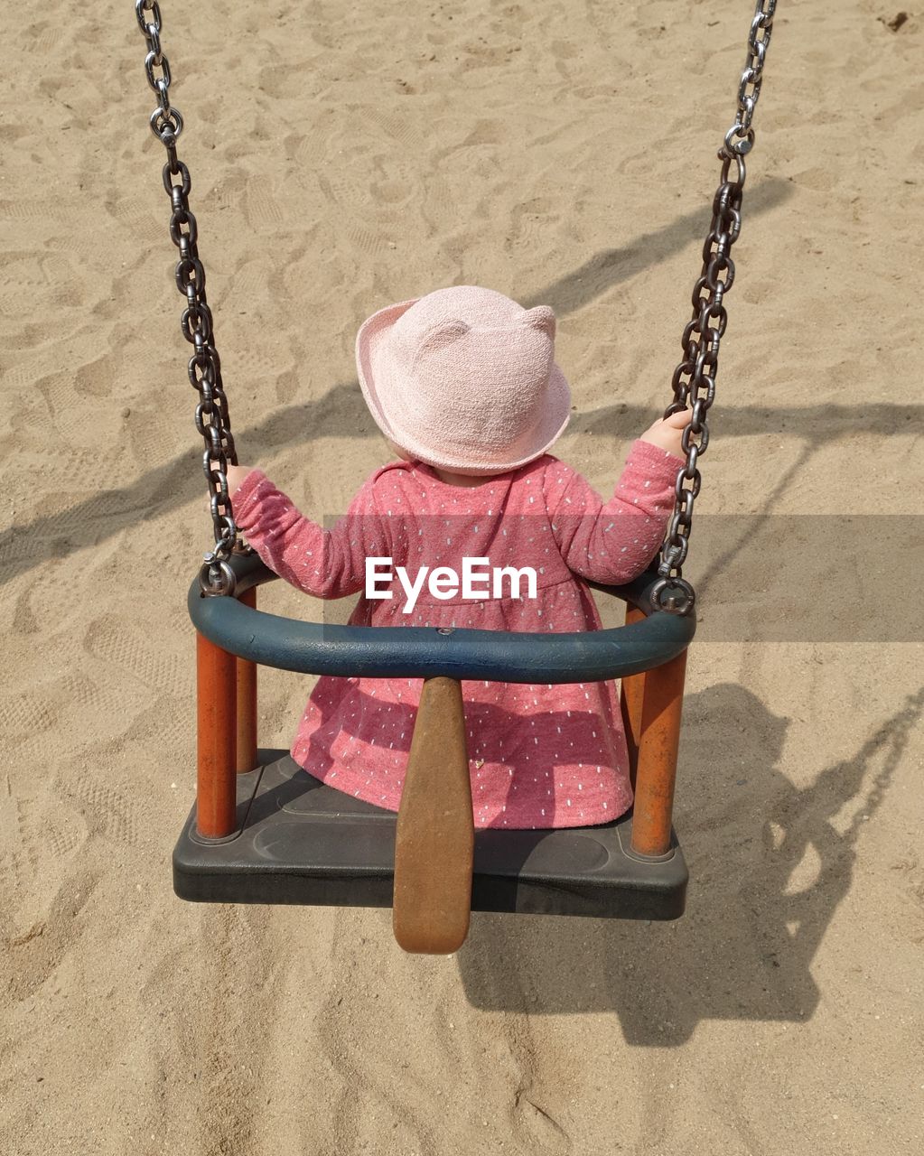 REAR VIEW OF CHILD SITTING ON SWING IN PLAYGROUND