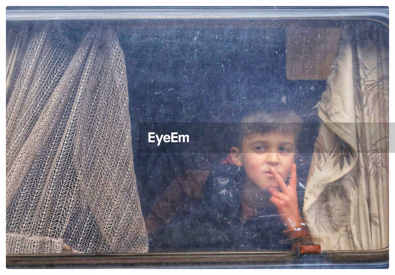 Boy gesturing while looking through window