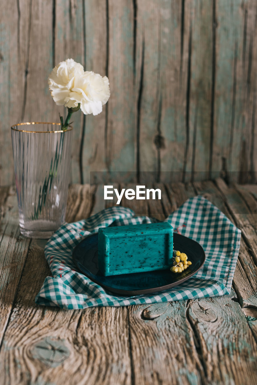 Plate with aromatic organic soap and flowers placed on napkin on shabby lumber table near cup with ingredient