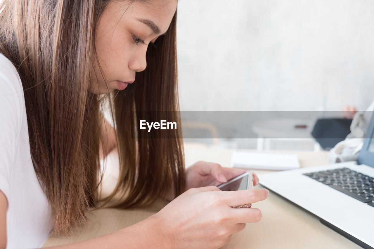 SIDE VIEW OF WOMAN USING MOBILE PHONE IN LAPTOP