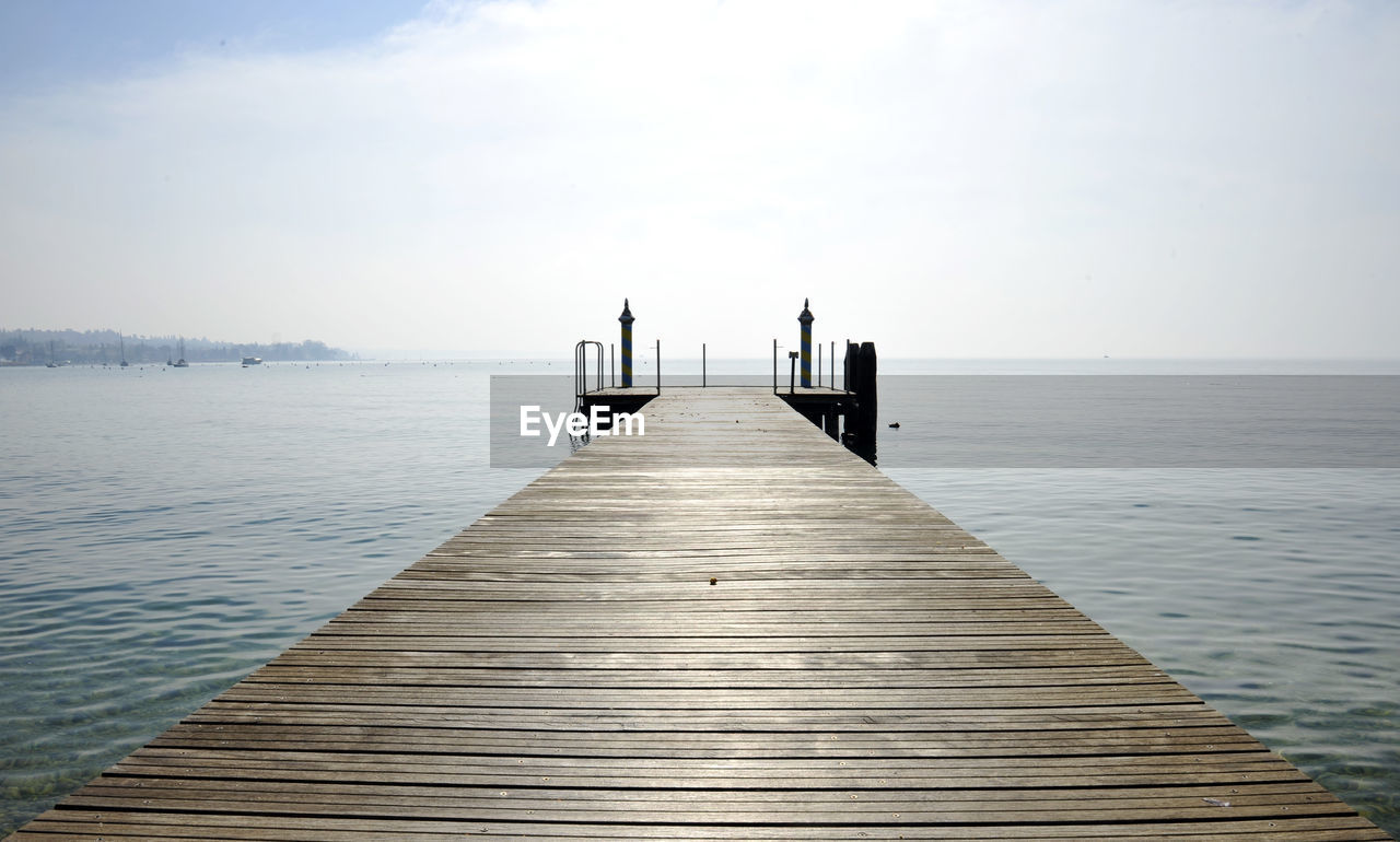 Wooden jetty leading to pier over sea against sky