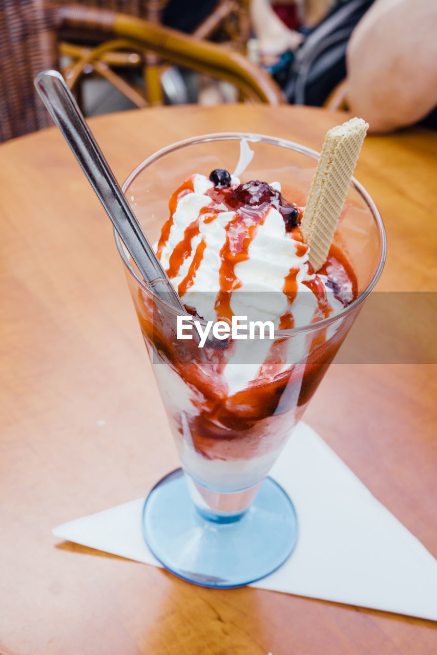 Ice cream with whipped cream and berry sauce in glass on table