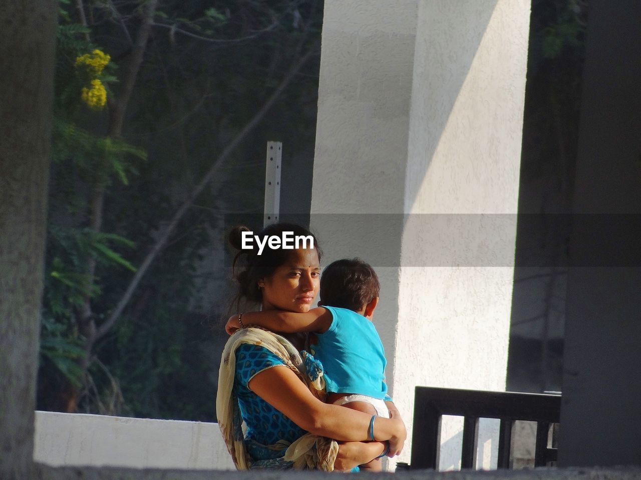 Thoughtful woman carrying child while standing on balcony