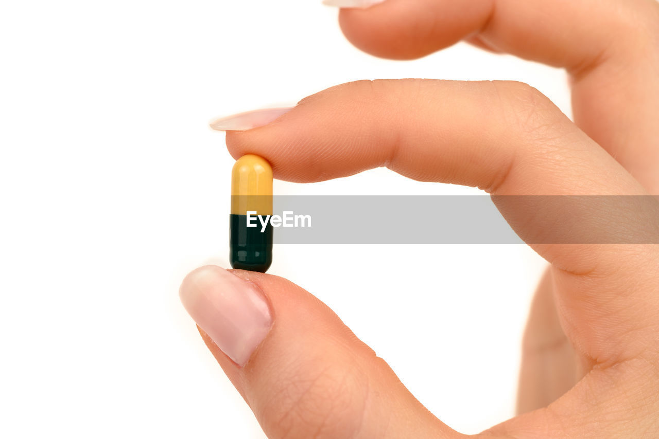 Close-up of hand holding pill over white background