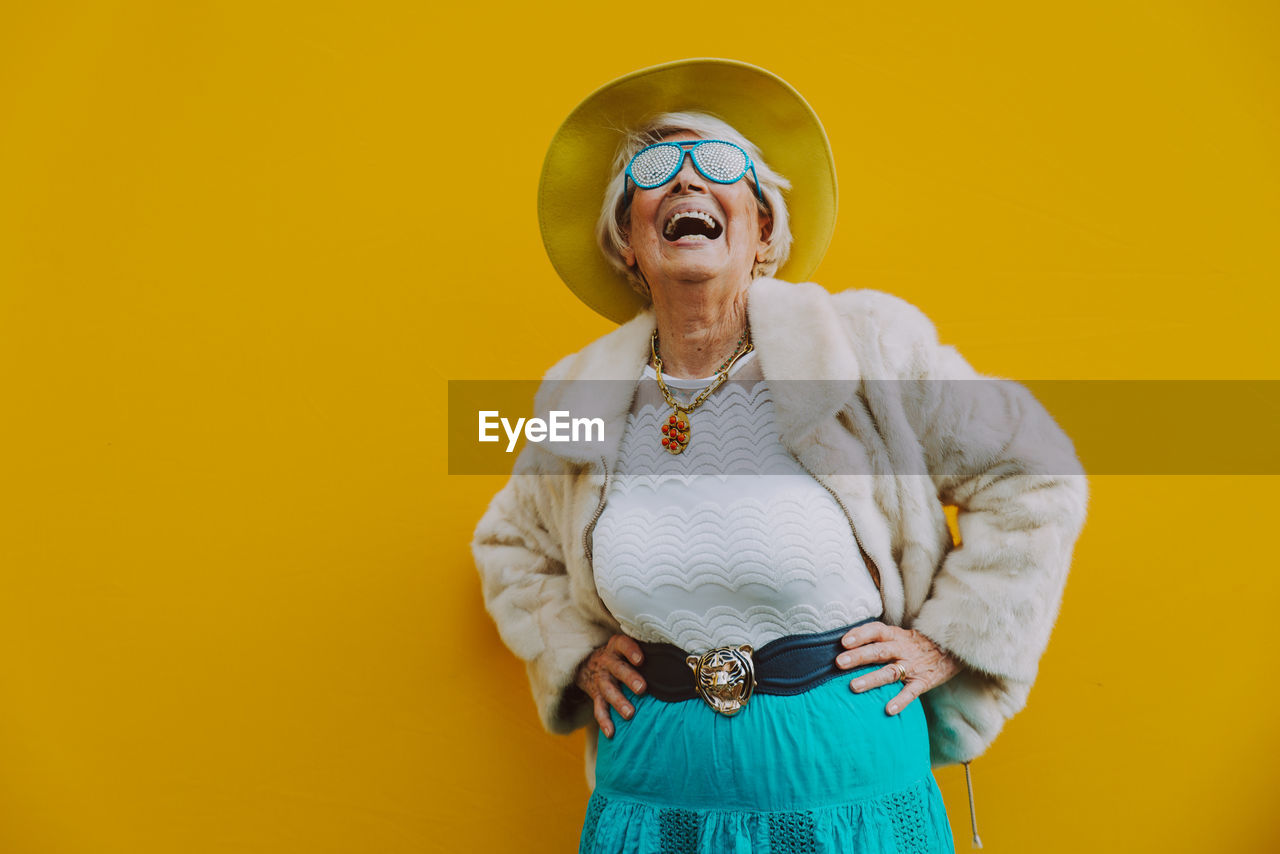 Cheerful senior woman standing against yellow background