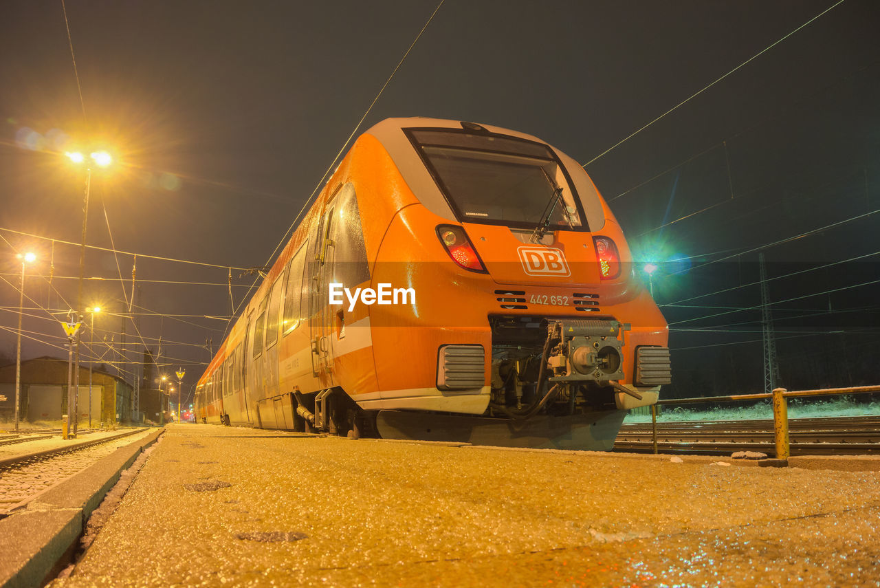 TRAIN AT RAILROAD STATION PLATFORM AGAINST SKY AT NIGHT