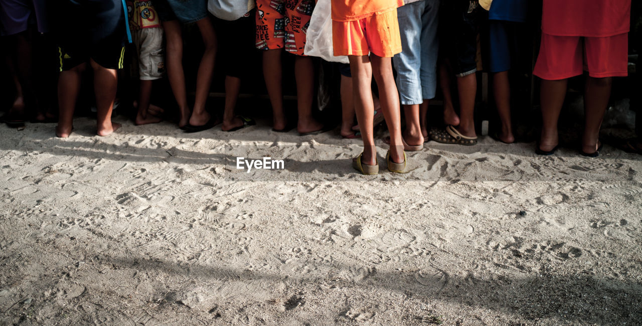 Low section of people standing on sandy beach