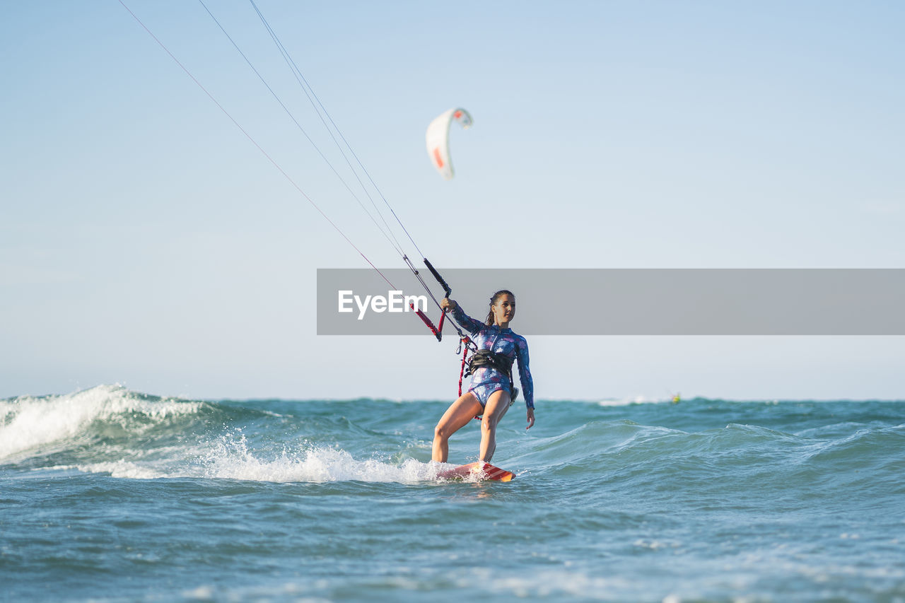 Fit female kite surfer in swimsuit ridding waves in sea on sunny day in summer