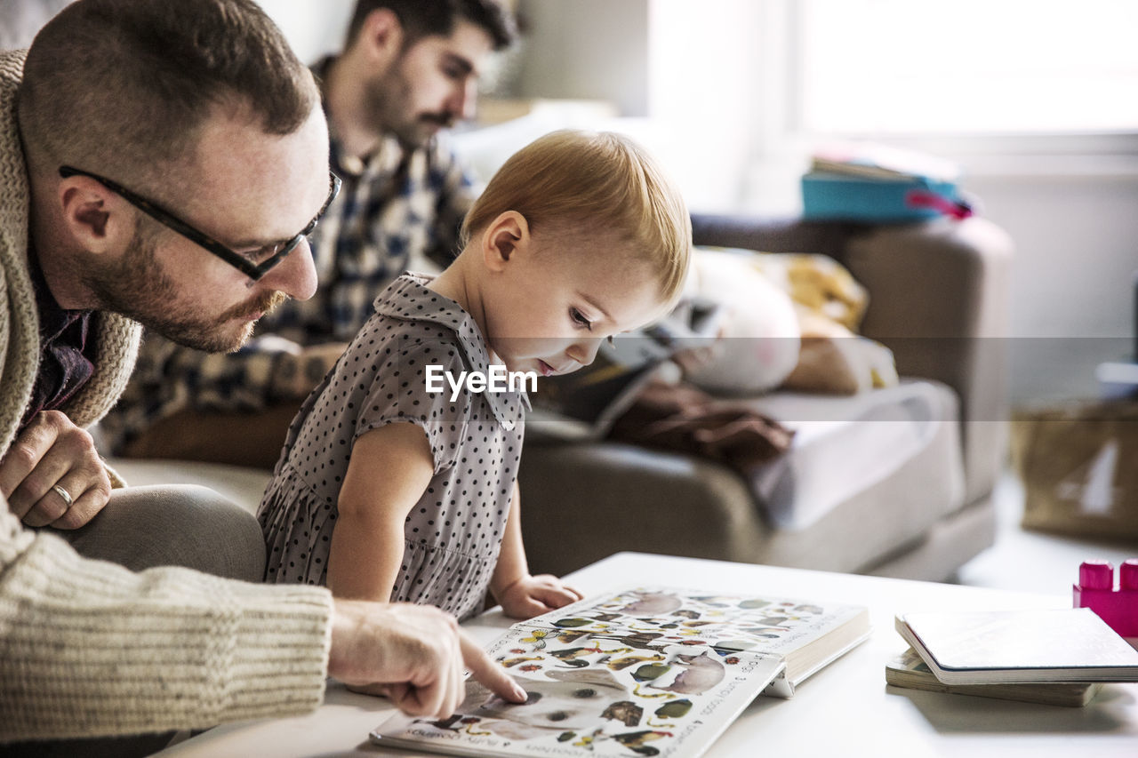 Father showing picture book to girl with partner sitting in background