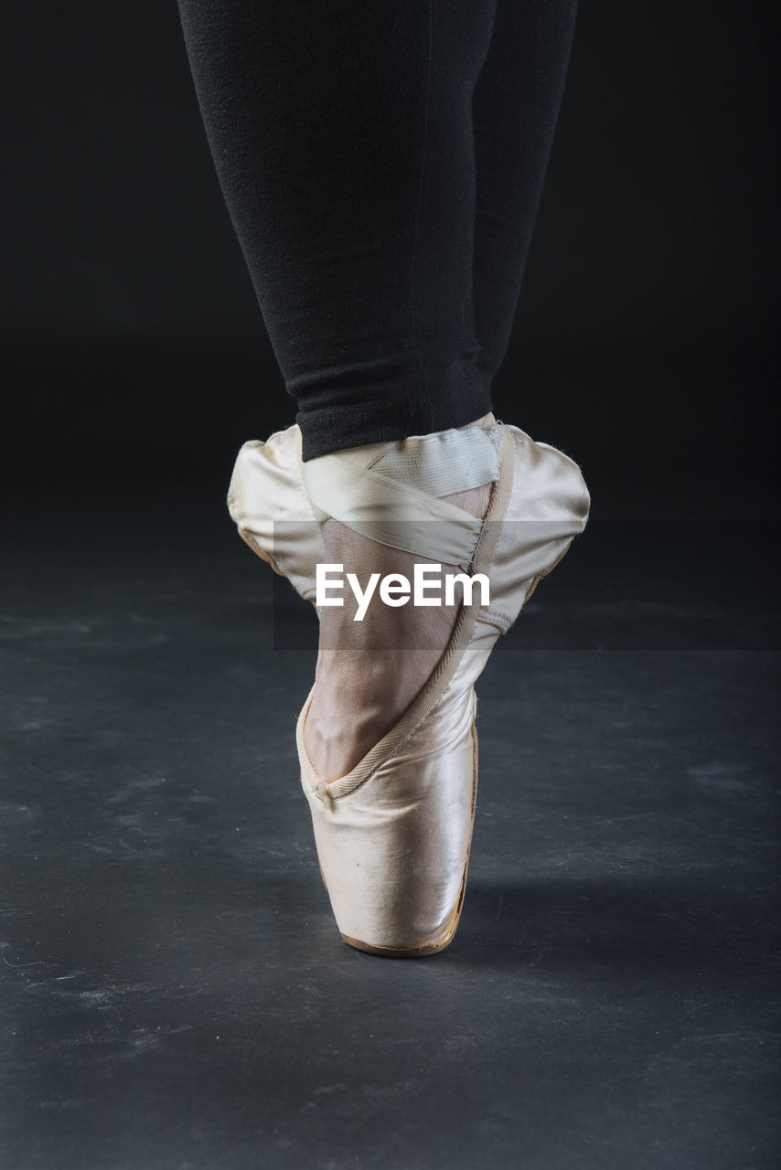 Low section of ballet dancer against black background