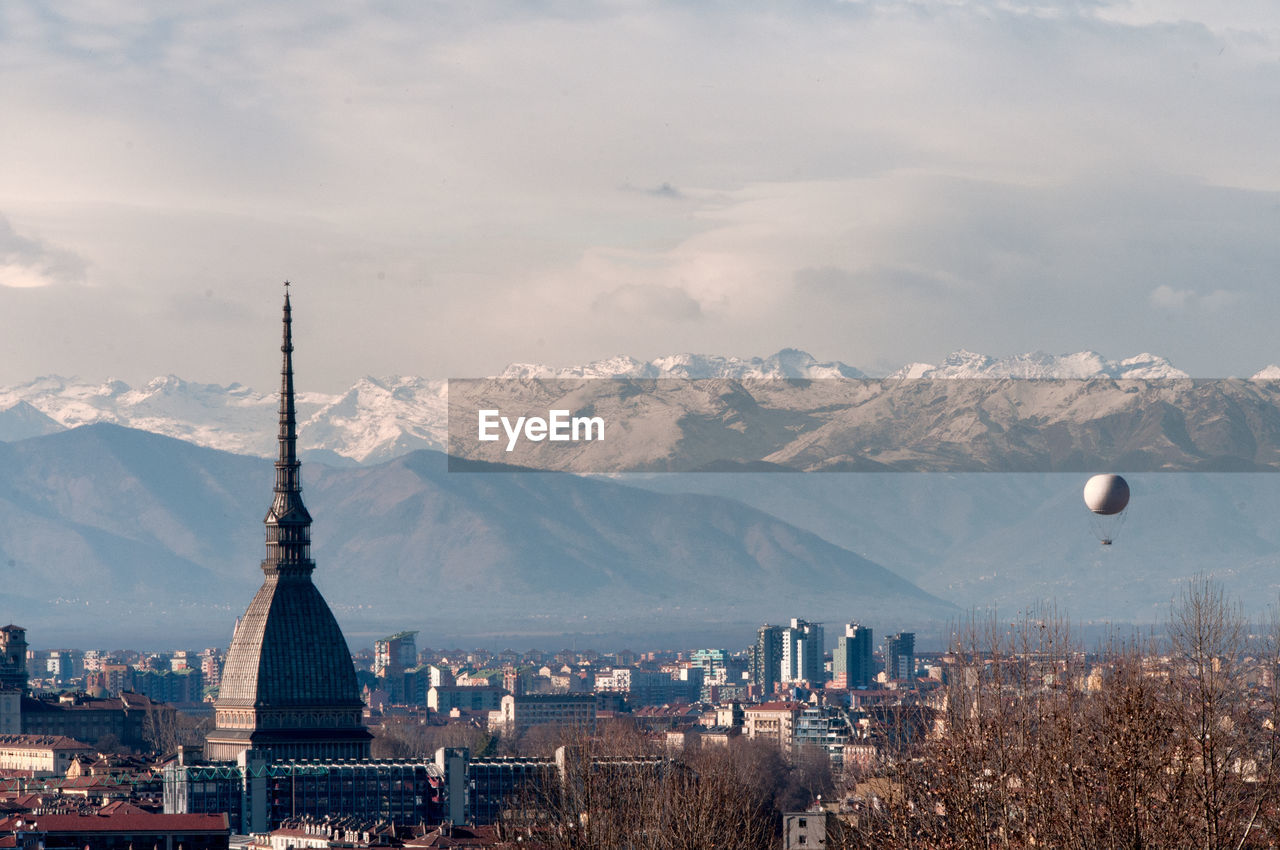 Old church in city by snow covered mountains against cloudy sky