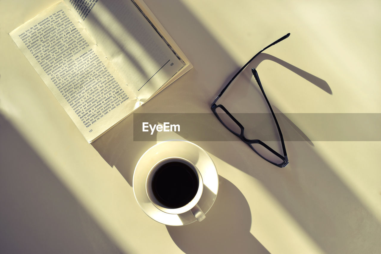 Directly above shot of coffee cup with eyeglasses and book on table